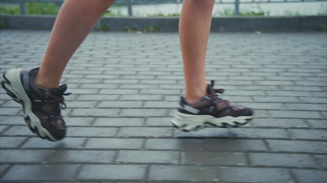 Feet move rhythmically on wet pavement. Shoes grip the ground with steady motion. Person runs along a paved outdoor path. Damp surface reflects recent rain. Energy and motion define this moment