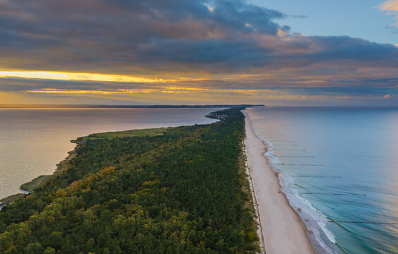 Aerial view of Hel Peninsula featuring the narrow sandy beach, dense pine forests, and calm waters of the Baltic Sea at sunset in Chalupy, Pomeranian Voivodeship, Poland.