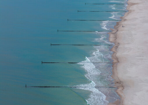 Aerial view of Hel Peninsula featuring wooden groynes extending into the Baltic Sea along the sandy coastline of Chalupy, Pomeranian Voivodeship, Poland.