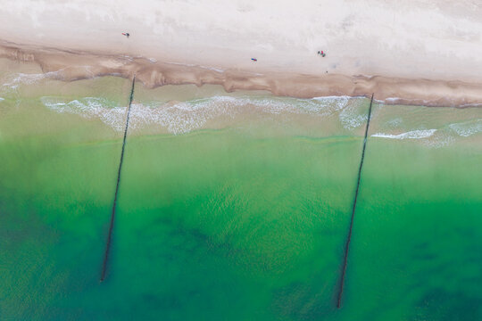 Aerial view of Hel Peninsula featuring sandy beach, turquoise sea water, and wooden groynes extending into the Baltic Sea in Chalupy, Pomeranian Voivodeship, Poland.
