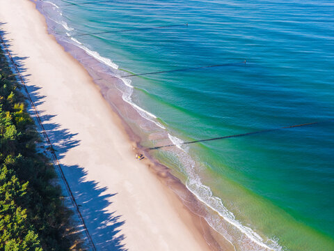 Aerial view of Hel Peninsula with sandy beach, clear Baltic Sea waters, and wooden groynes extending into the sea, bordered by forest in Chalupy, Pomeranian Voivodeship, Poland.