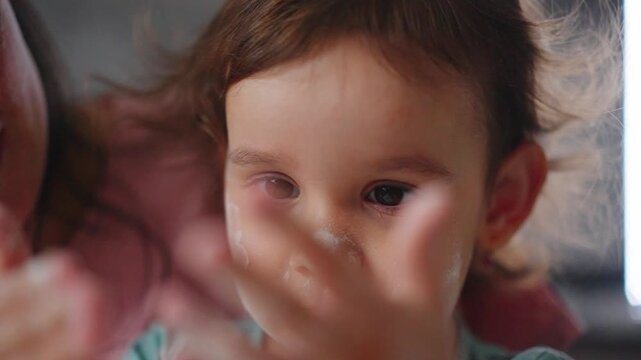 Child smiles with frosting on nose, hands raised. Mother smiles close, giving thumbs-up. Joyful messiness captured, playful moment preserved. Perfect for parenting, childhood, or fun family content