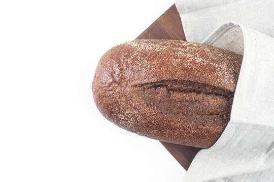 Dark bread loaf on a wooden cutting board with a fabric napkin against a white background. Bakery product with textured crust and copy space for food advertising, packaging design and grocery banners.
