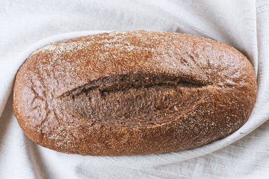 Top view of dark sourdough rye bread loaf dusted with flour lying on linen cloth background. Artisan bakery, organic whole grain bread, traditional baking and food staging concept.