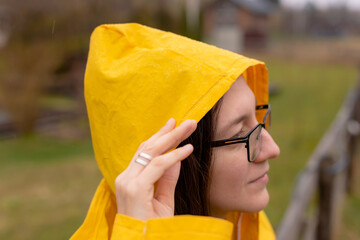 Close-up profile woman in yellow raincoat adjusting hood in rainy weather © cenchild