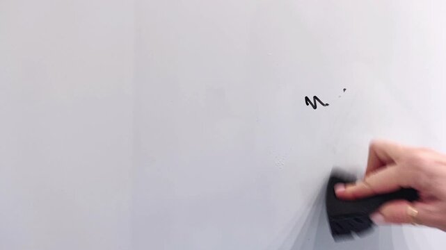 Female hand erases black marker lines from a whiteboard using a new black cleaning sponge, leaving a clean surface, office cleaning, horizontal video.