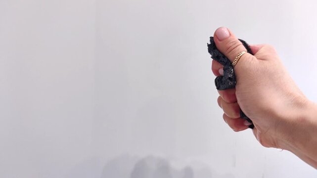 Female hand squeezes a wet black cleaning sponge as water drips from its porous surface, close-up demonstration of absorbency, household cleaning, horizontal video.
