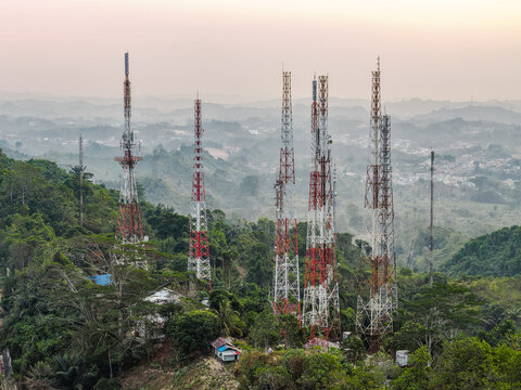 Aerial view of television broadcasting station with multiple tall metal towers rising above lush green hills and tropical forest under a soft hazy sky in Samarinda, East Kalimantan, Indonesia.
