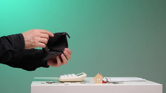 Person's hands holding an empty brown wallet, illustrating financial difficulties, debt, and the struggle to afford housing, with house keys and scattered coins on a table