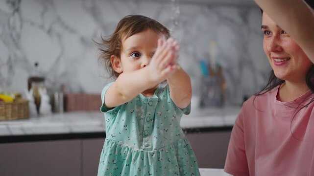 Mother and child share joyful kitchen moment. Little girl playfully blows flour into air. Woman laughs, eyes closed, in loving gesture. Warm, playful mood perfect for family content