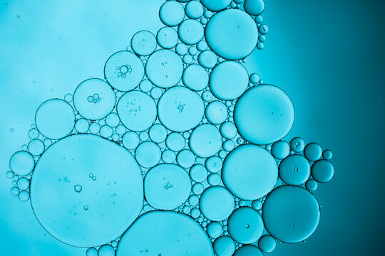 Blue oil bubbles floating in clear liquid close up view