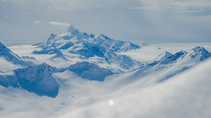 Snow-covered Mount Elbrus and surrounding Caucasus ridges rising above clouds in blue winter daylight © ossyffer
