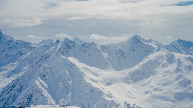 Snow-covered Caucasus Mountain peaks under cloudy sky panoramic aerial view of alpine ridges and glaciated slopes