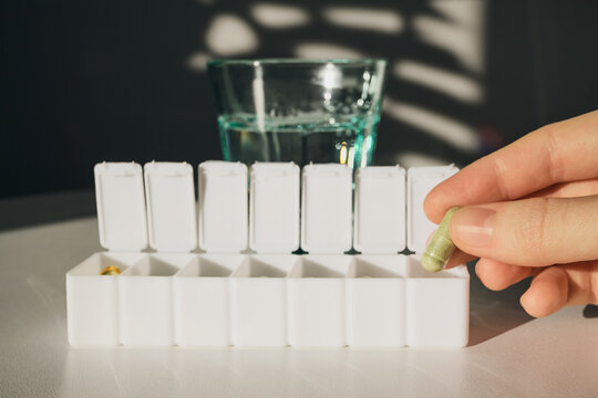 Woman removing capsule from pill organizer for medication intake