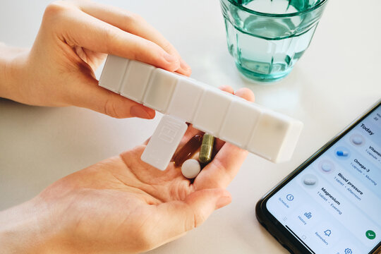 Woman tracking medication intake with smartphone app and weekly pill organizer