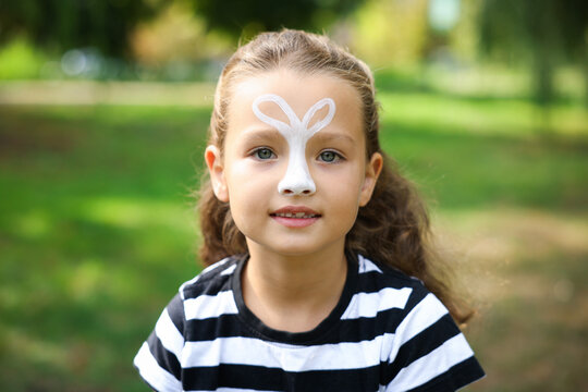 Little girl with bunny painting on her face outdoors
