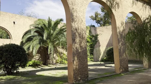 Barcelona, Spain, October 13, 2026 - Historic arcaded gallery with a series of stone arches in Jardins de l'Umbracle on Montjuic hill, surrounded by lush garden vegetation.