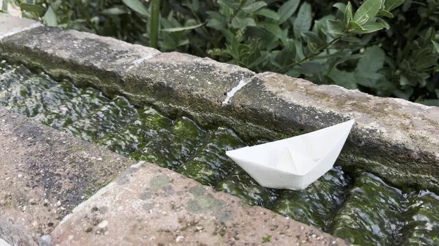 A little paper boat rests near an ancient millstone as water trickles down its surface in one of the historic gardens on Montjuic hill in Barcelona, Spain.