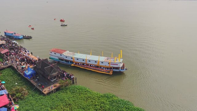 Tenggarong, Indonesia - 27 September 2026: Aerial view of the Ngulur Naga Erau boat on the Mahakam River with crowds gathered on the wooden pier during the festival.