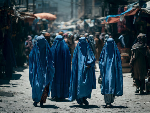 Women wearing blue full body coverings walking through a crowded market street with vendors, pedestrians, and urban buildings in Afghanistan