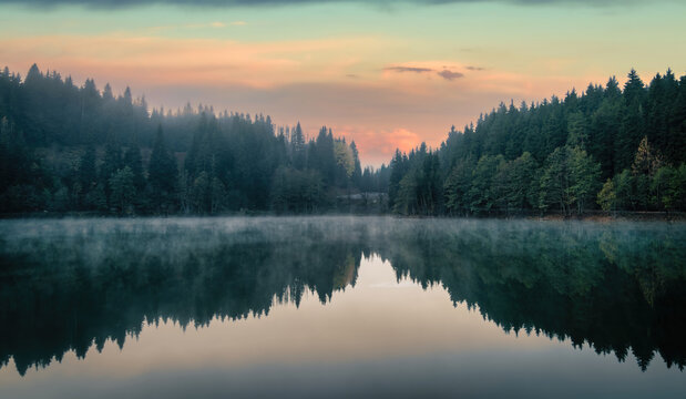 Karagol lake in Savsat, Artvin, Turkey, at dawn with a pink and orange sky, fog over the water and dark fir forest mirrored on the calm surface