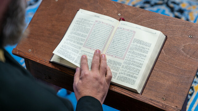 Imam reading the Quran with Turkish translation on a wooden lectern during Ramadan in a small mosque in Savsat, Artvin, Turkey, close-up of his hand on the holy book