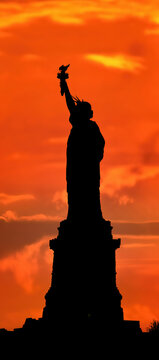 Statue of Liberty in New York, USA, in silhouette against a fiery red and orange sunset sky