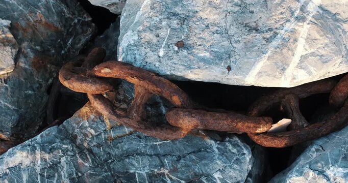 Rusty chain links between coastal rocks in close up