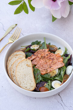 Lunch with salmon, salad, and bread on a white table with a flower in the background
