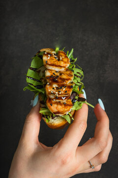 Shrimp sandwich with greens held in a hand against a dark background