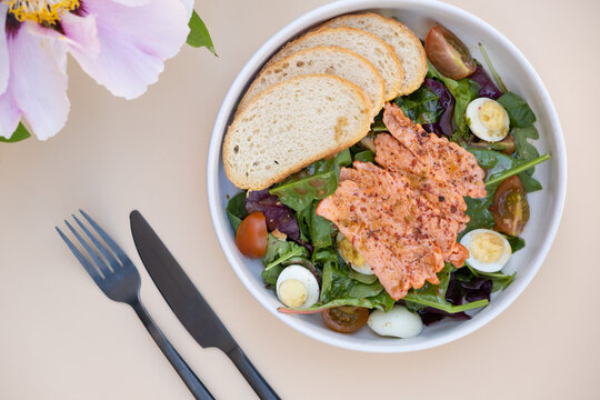 Salad with salmon, bread, and vegetables at a dining table with a flower in the background