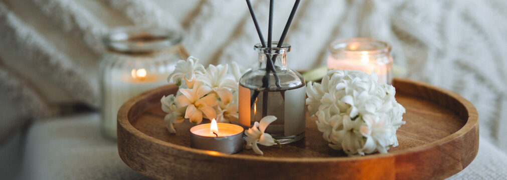 Banner. Home comfort, coziness, aromatherapy. Cozy interior with knitting, burning candles and aroma perfume diffuser in the living room. Fresh spring blossom fragrance, white hyacinth