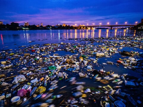 Blue hour long exposure plastic waste river, river choked with plastic debris at twilight, environmental pollution fine art photography, plastic river biodiversity crisis editorial