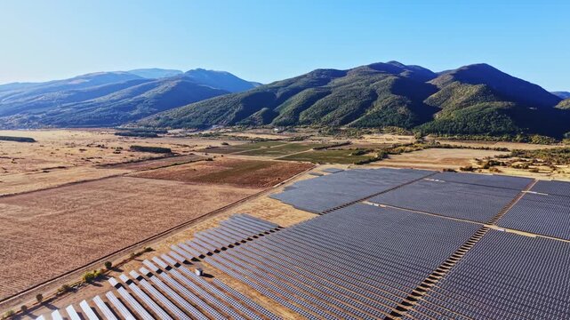 Solar panels stretch across the landscape in a valley near mountains, showing the use of renewable energy in agriculture. The scene is set during a clear day.