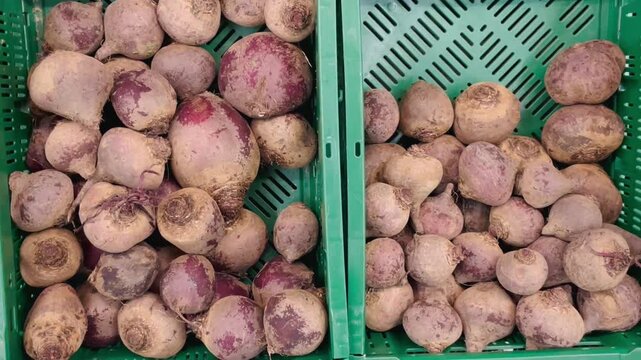 Close-up view of unwashed red beets piled in green plastic market crates on retail produce shelf, showing dirt-coated skins, round irregular shapes.