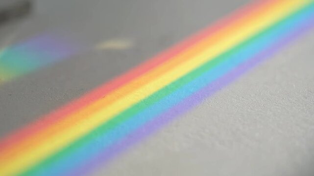 A rainbow band of refracted light falls across a soft white surface. A concept of diversity and inclusion and optimism for pride and education and minimal brand backgrounds.