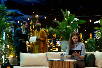 Businesswoman, tablet and digital work as seated professional studies a handheld screen in rooftop lounge at night. Productivity, project review and mobile technology suit focused business tasks. © DC Studio