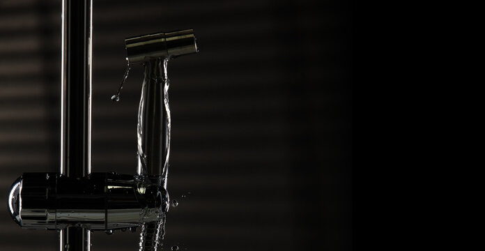 Bidet shower head leak water from hoses plumbing in bathroom as water clogged drop. Black background isolated. Leaking water from chromium stainless steel bidet shower head