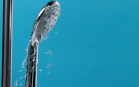Shower head leak water from hoses plumbing in bathroom as water clogged drop. Blue bathroom  background isolated. Leaking water from chromium stainless steel shower head