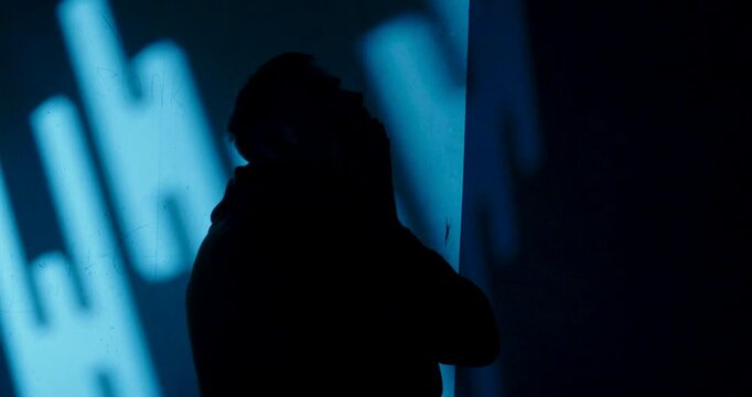 Hooded man holding his head in distress in a dark blue room