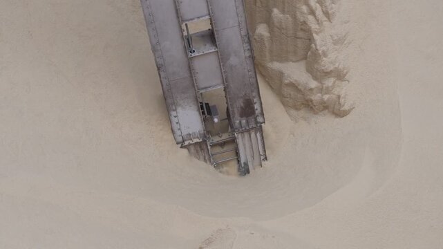 high angle view into the cargo hold of a bulk carrier ship showing a pneumatic suction unloader commencing discharge operations of dry bulk rice grain