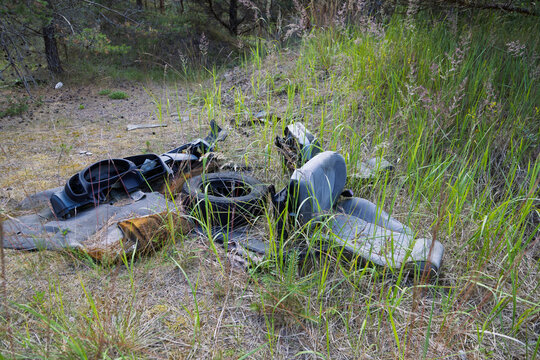 Discarded car parts including a dashboard, a tire, and a seat lie abandoned in a grassy field.