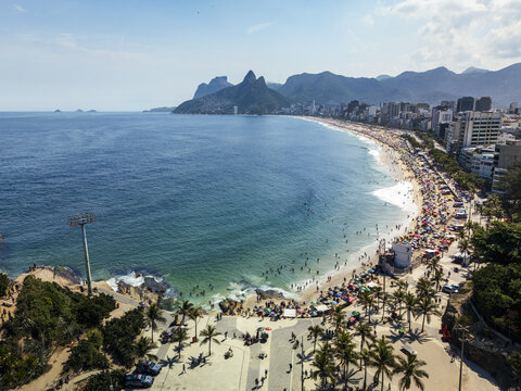 Aerial view of Ipanema Beach with crowds on the sand, turquoise ocean, palm trees along the promenade, and Two Brothers mountains in Rio de Janeiro, Rio de Janeiro, Brazil.