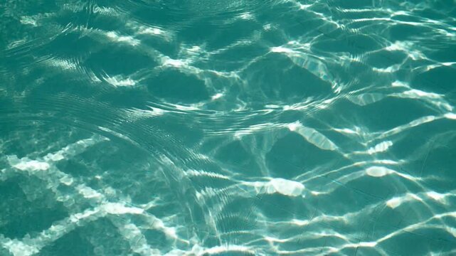 Turquoise swimming pool water surface with shimmering sunlight caustics and gentle ripples, a refreshing summer and vacation background