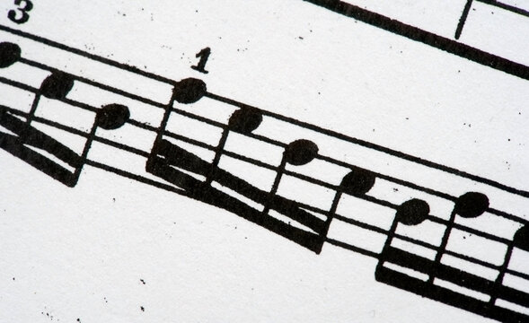 Closeup of printed sheet music, black musical notes on white paper, five-line staff with beamed eighth notes, measure numbers, classical music notation detail, diagonal composition