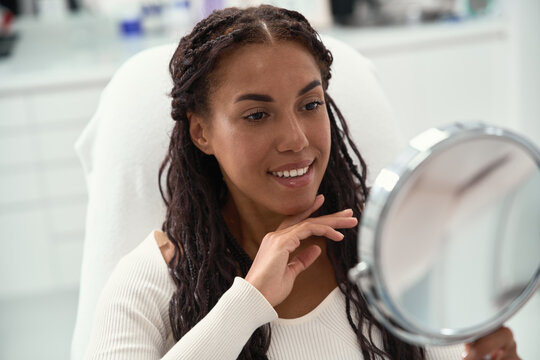 Cosmetic dentistry smile aesthetics highlight white teeth and natural dental alignment. Smiling African woman rests manicured fingertips on her cheek in a detailed facial closeup.
