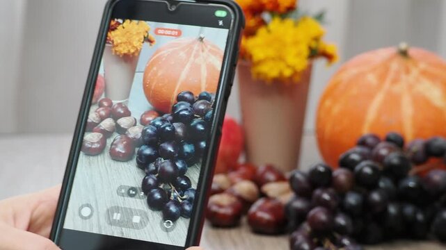 Autumn Thanksgiving arrangement, still-life, smartphon. Harvested pumpkins, a beautiful bouquet of yellow and orange flowers, fruits and vegetables, autumn leaves, and red berries on a wooden table. A