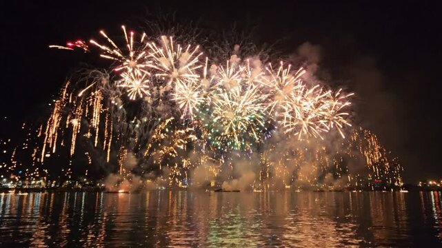 Fireworks display exploding over water at night with reflections