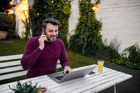 Man works on laptop and talks on phone in garden during afternoon