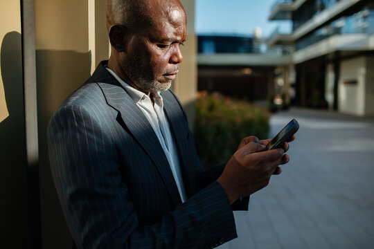 Senior businessman texting on smartphone outside office building